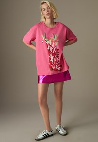 Lyserød oversized t-shirt med grafik af en dekoreret vinterstøvle og teksten "Rodeo" i sort. Kombineret med en skinnende magenta mini-nederdel.