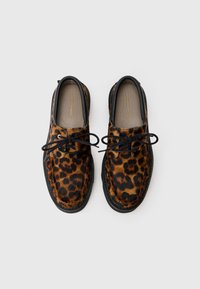 Sko med leopardprint og en pelsagtig tekstur, sorte detaljer, rund tå og sorte snørebånd. Har en flad sål og diskret branding indeni.