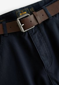 Dunkelblaue, strapazierfähige Baumwollshorts mit einem braunen Ledergürtel. Ausgestattet mit einer Metallschnalle, genähten Nähten und einem Etikett im Bund.