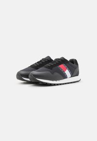 Sneaker nere con un mix di pelle e tessuto, dotate di un'intersuola bianca e strisce rosse, bianche e blu sul lato.