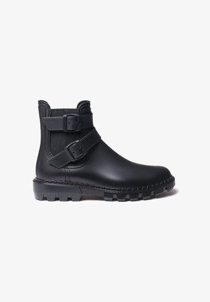 Zwarte enkelboot gemaakt van glad rubber met twee gespsluitingen, gestructureerde bovenkant, versterkte stiksels en een robuuste zool met grippatroon.