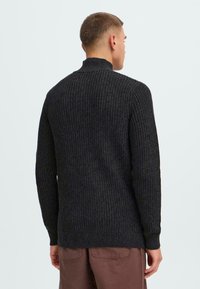 Schwarzer, gerippter Strickpullover mit hohem Kragen, der ein strukturiertes Muster und lange Ärmel aufweist, von hinten betrachtet.