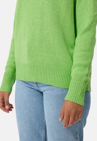 Gehaakte trui in felgroen, met ribgebreide manchetten en zoom. Gecombineerd met lichtblauwe jeans, die een ontspannen pasvorm en zachte textuur hebben.