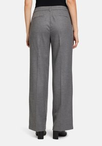 Pantalons larges gris en tissu texturé, avec des poches arrière et une ceinture plate, associés à des bottines à talons noires.