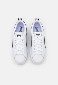 Baskets blanches avec un dessus en cuir texturé, des accents noirs sur les côtés, des lacets plats et une languette rembourrée avec un détail du logo de la marque.