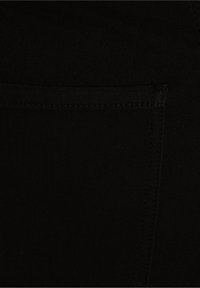 Mustan joustavan housukankaan materiaali, jossa on näkyvä takatasku ja erottuva ommel. Sileä tekstuuri ja tiukasti istuva muotoilu.