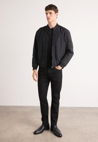 Svart bomberjakke med glidelås, ribbet krage og mansjetter, kombinert med svarte slim-fit bukser og svarte dressko.