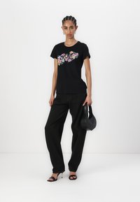 Black short-sleeve t-shirt with floral graphic, paired with loose black pants and high-heeled sandals; holding a black handbag.