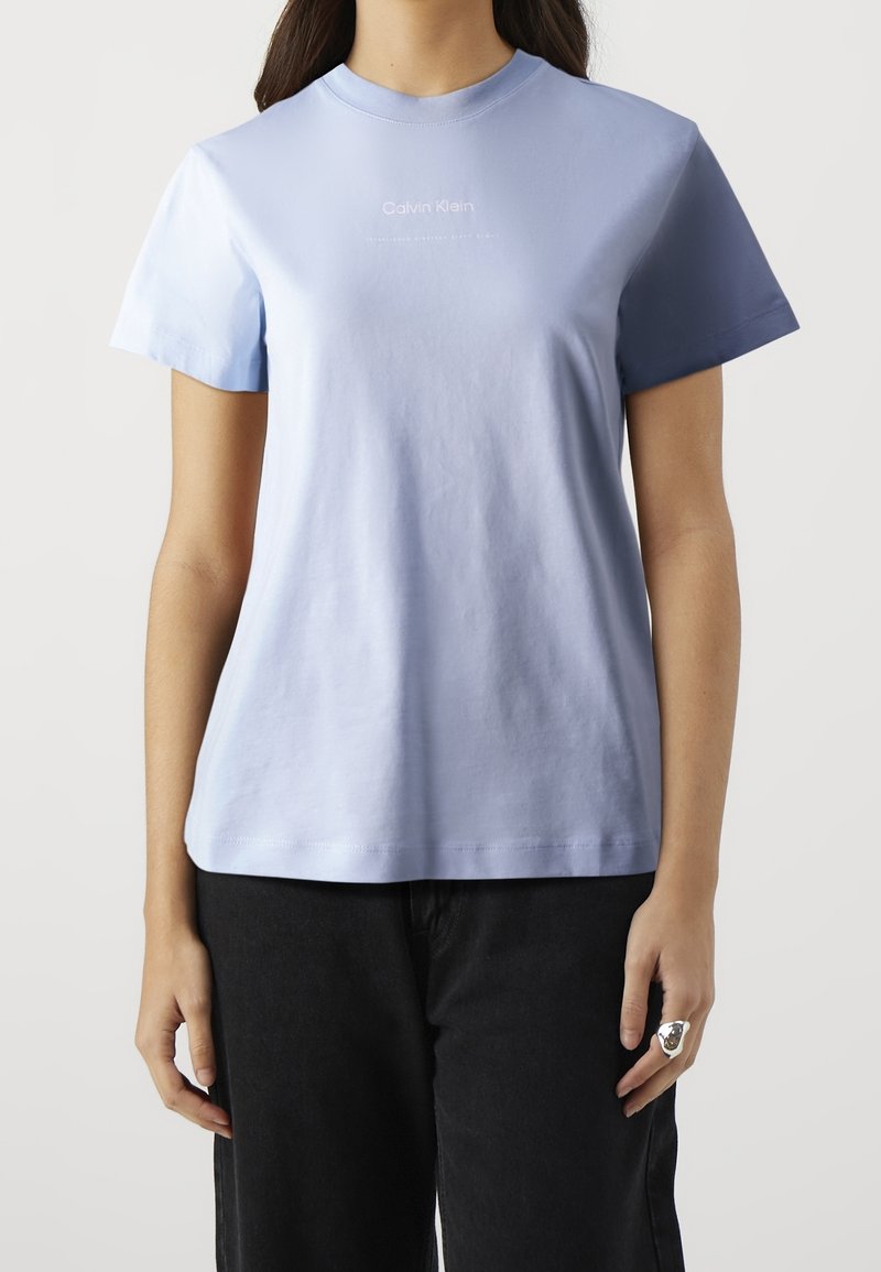 Světle modré bavlněné tričko s krátkými rukávy, kulatým výstřihem a bílým logem "Calvin Klein" na přední straně. Hladká textura, uvolněný střih.