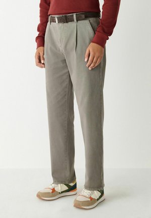 Light gray pleated trousers made from soft fabric, featuring a brown belt. Paired with multicolored sneakers displaying a retro design.