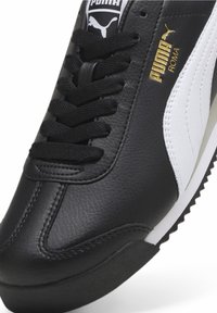 Baskets Puma Roma en noir et blanc avec dessus en cuir, lacets noirs, logo doré et semelle en caoutchouc texturée. Présentent un design sportif classique.