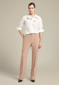 Witte overhemd met zilveren versieringen op de kraag, gecombineerd met beige cargobroek met zijkrekken en zwarte hakken.