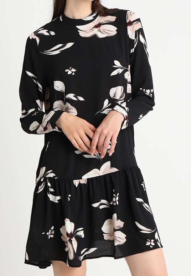 Robe noire à manches longues, motif floral en rose pâle et crème. Présente un ourlet volanté et un tissu léger pour une silhouette fluide.