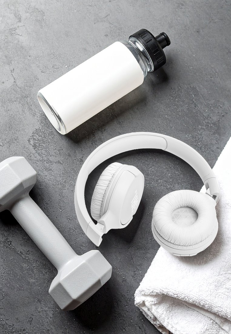 Weißes Over-Ear-Headset mit weicher Polsterung, eine graue Hantel, eine klare Wasserflasche mit schwarzem Deckel und ein weißes Handtuch auf einer dunklen Oberfläche.