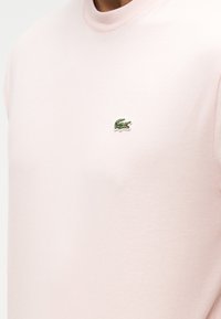 T-shirt rose clair à col rond avec petit logo crocodile vert brodé sur le côté gauche de la poitrine.