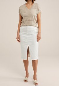 Beige stickad v-ringad topp med korta ärmar, kombinerad med en vit midikjol med slits framtill, och beiga blommiga slip-in sandaler.