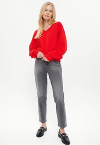Felpa rossa oversize con collo a V, abbinata a jeans grigi a vita alta e mocassini neri con dettagli in oro.