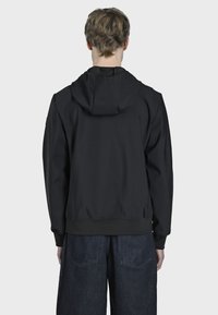 Crna zip-up hoodie s pripijenim siluetom, podešavanom kapuljačom, teksturiranim materijalom i rebrastim manžetama. Uparen s širokim tamnim trapericama.