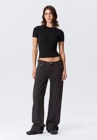 Schwarzes, eng anliegendes T-Shirt kombiniert mit weiter geschnittenen grauen Jeans. Die Jeans haben eine hohe Taille und dezente Nahtdetails, ergänzt durch schwarze Schuhe.