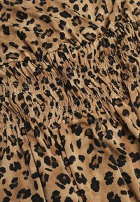Tissu imprimé léopard avec un fond beige et des taches noires. Détails de smocks élastiques qui améliorent la texture et la forme du matériau.