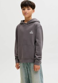 Felpa grigia con tasca frontale, cappuccio e logo bianco. Abbinata a jeans baggy blu chiaro. Tessuto morbido, vestibilità casual.