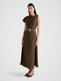 Oliwkowa, bezrękawnikowa sukienka z drapowanym materiałem, paskiem z złotą klamrą i zwiewnym dołem. Noszona z brązowymi szpilkami.