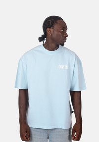 Světle modré bavlněné tričko s krátkými rukávy, oversize střih a bílé nápisy "CRYSTAL" na levé straně hrudi. Obsahuje kulatý výstřih.