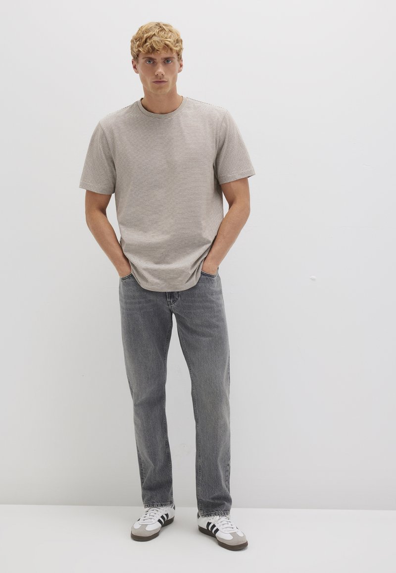 Striped short-sleeve t-shirt in beige, paired with gray straight-leg jeans. Worn with white sneakers featuring black and gray accents.