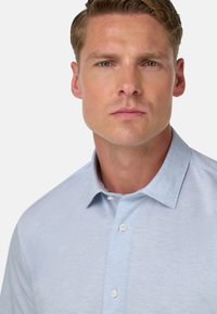 Hellblaues, kurzärmliges Hemd mit Knopfleiste aus strukturiertem Stoff; verfügt über einen klassischen Kragen und zwei Knöpfe an der Vorderseite.