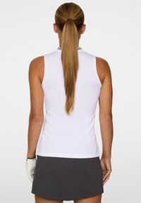 Vit ärmlös polo med hög krage och svarta accenter, i kombination med en mörkgrå kjol. Slät tygtextur, figurnära design.