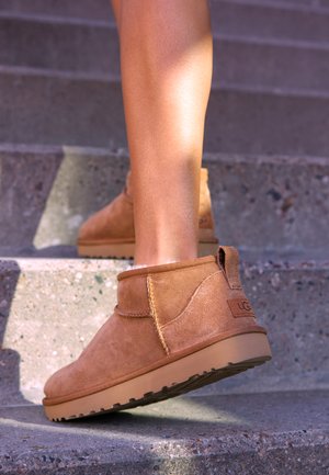 Tan suede ankle boots with a soft texture, stitched detailing, and a rubber sole, featuring a looped heel for easy wear.