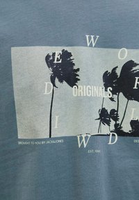 Grafisk t-shirt i blå med et print af palmer i sort, med tekstelementer "WORLD" og "ORIGINALS" i hvid. Blødt bomuldsstof.