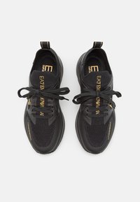 Svarta träningsskor med övre i nät, rund tå och tjock sula. Har guld accenter och snören för en säker passform.