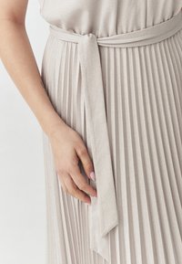 Abito plissettato grigio chiaro con texture in satin. La vita è cin cinata con una cintura in tessuto abbinato, caratterizzata da una finitura liscia e una vestibilità comoda.