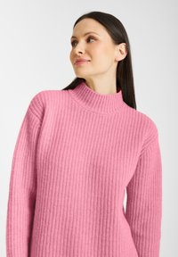 Różowy sweter z prążkowanego materiału o wysokim dekolcie i długich rękawach. Miękka tekstura z luźnym krojem. Minimalistyczny design, bez widocznych wzorów czy ozdób.