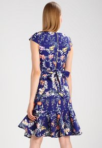 Blommig klänning i marinblått tyg med korta ärmar. Har en figurnära liv, bakband och volangkant nedtill.