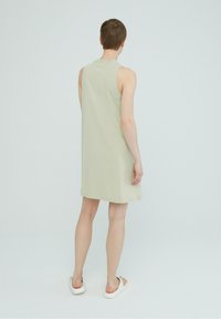 Ljusgrön ärmlös klänning i mjukt tyg, lös passform, knälång, med en enkel design; bärs med vita slip-on skor.