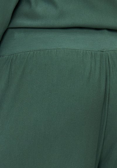 Green fabric close-up, featuring a smooth texture with a ribbed elastic waistband. The material is soft and stretchy, with subtle folds.