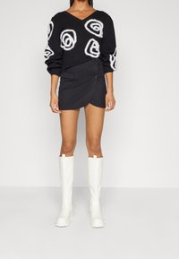 Black sweater with white spiral patterns, paired with a black wrap skirt and white knee-high boots. Smooth fabric and structured design.