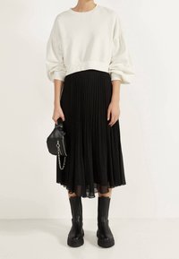 Maglione bianco con maniche a palloncino, abbinato a una gonna midi plissettata nera. Stivaletti neri alla caviglia e una piccola borsa nera con dettaglio a catena.