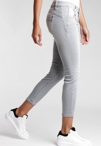 Jeans skinny de denim gris con una cintura de media altura, que cuentan con un diseño de cinco bolsillos, pasadores para el cinturón y piernas ajustadas, combinados con zapatillas blancas.