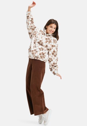 Pull en polaire avec un motif floral blanc et marron, associé à un pantalon large marron et des baskets légères, comportant une fermeture éclair mi-hauteur.