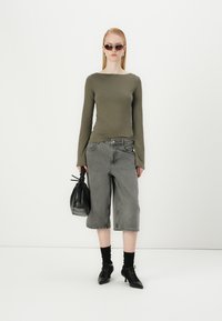 Maslinasti dukserica dugih rukava, sivi traper culottes, crna torba, crne čarape, crne cipele s pointama, minimalistički dizajn, glatke teksture i neutralne boje.