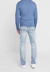 Blå tröja med ribbade ärmslut, i kombination med ljusblå jeans som har dubbel bakfickor och en slim-fit design. Vita skor fulländar looken.