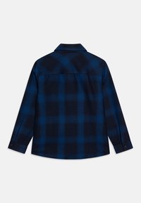 Camicia di flanella blu navy con un motivo a quadri che presenta quadrati blu scuri e chiari, maniche lunghe e colletto con scollo.