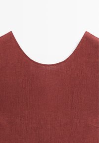 Nahaufnahme eines strukturierten, rostfarbenen Stoffes mit einem weiten, abgerundeten Ausschnitt, der ein detailliertes Webmuster zeigt.