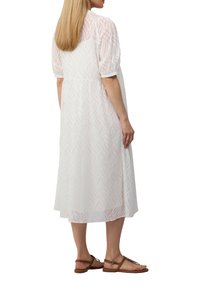 Vestido blanco de longitud media con un patrón de olas, mangas abullonadas y un ajuste holgado. Combinado con sandalias marrones de tiras.