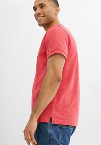 T-shirt di cotone corallo con maniche corte, collo rotondo, aperture laterali all'orlo e vestibilità rilassata, abbinata a jeans in denim blu.