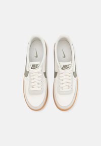 Baskets blanches Nike avec logos swoosh verts, semelles en caoutchouc naturel et lacets blancs, vues de dessus sur un fond clair.