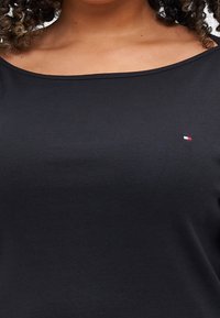 Musta, ribattu kangastoppi, jossa on leveä pääntie. Siinä on pieni, punaisella, valkoisella ja sinisellä ommeltu logo vasemmassa rintakohdassa.